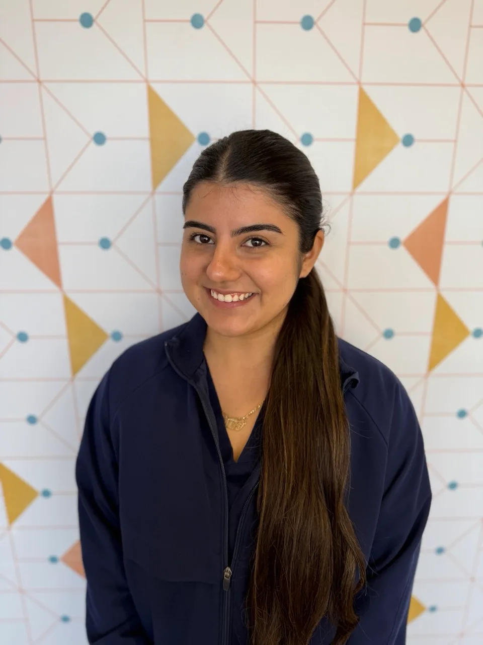 Poppy Kids dental assistant Alexandra, smiling in her uniform in front of a patterned wall.