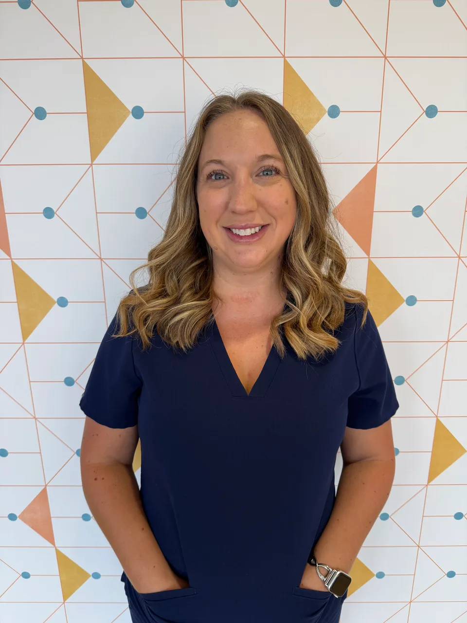 Poppy Kids front office admin Emily, smiling in her uniform in front of a patterned wall.