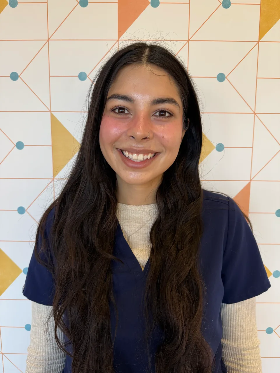 Poppy Kids patient comfort specialist Jen, smiling in her uniform in front of a patterned wall.