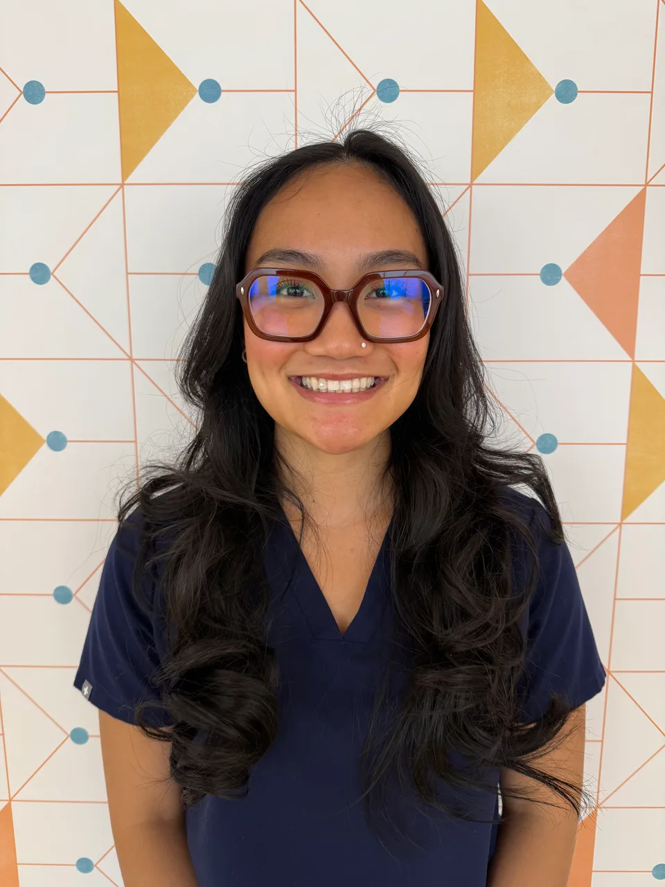 Poppy Kids front office admin Neah, smiling in her uniform in front of a patterned wall.